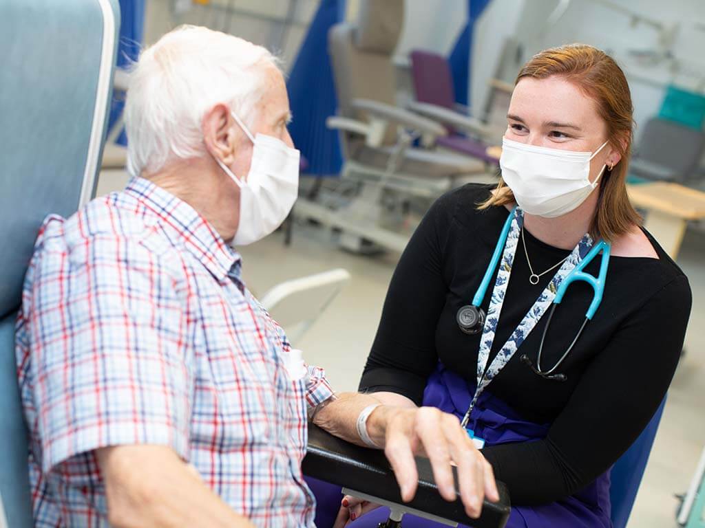 Consultant speaking with an elderly patient both wearing masks